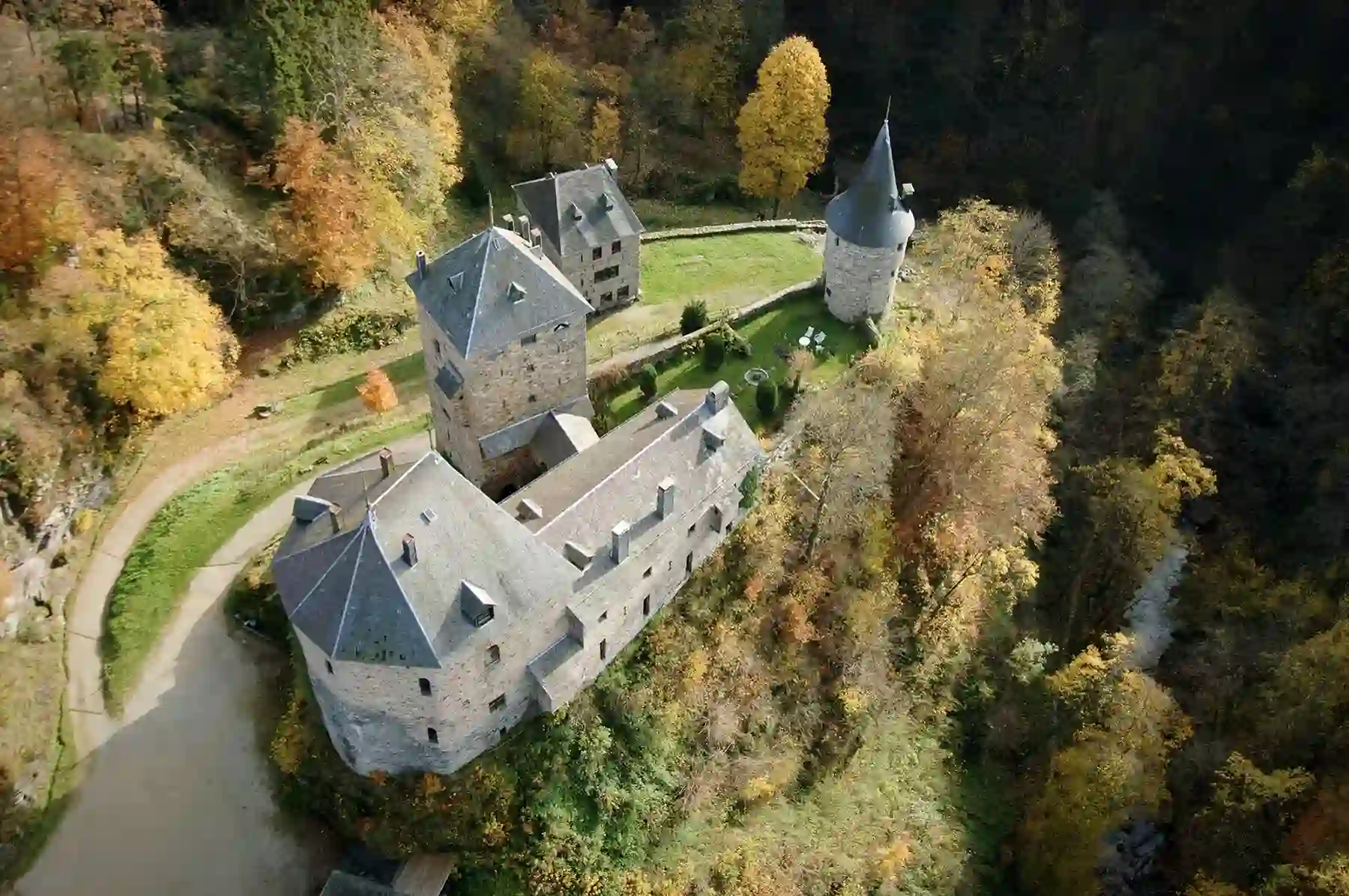 Vue aérienne du château de Reinhardstein sur son éperon rocheux, entouré d’une forêt aux teintes automnales