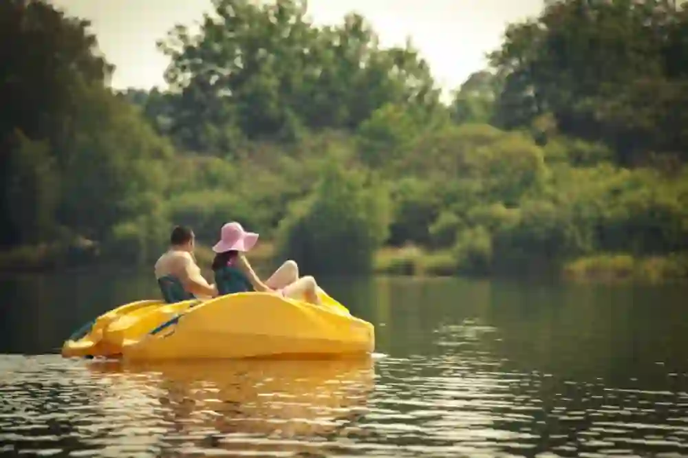 Un couple sur un pédalo jaune glisse sur les eaux calmes du lac, bordées d’arbres