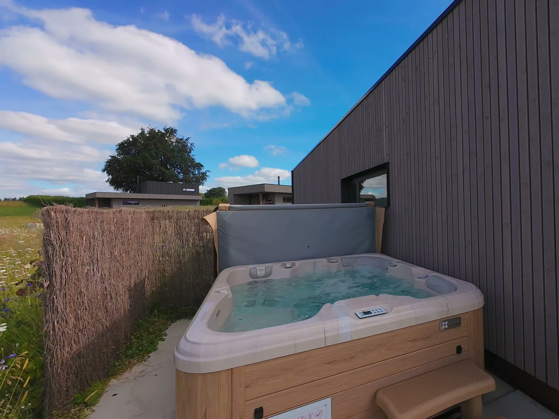 Jacuzzi extérieur bouillonnant, terrasse en bois face à la prairie fleurie