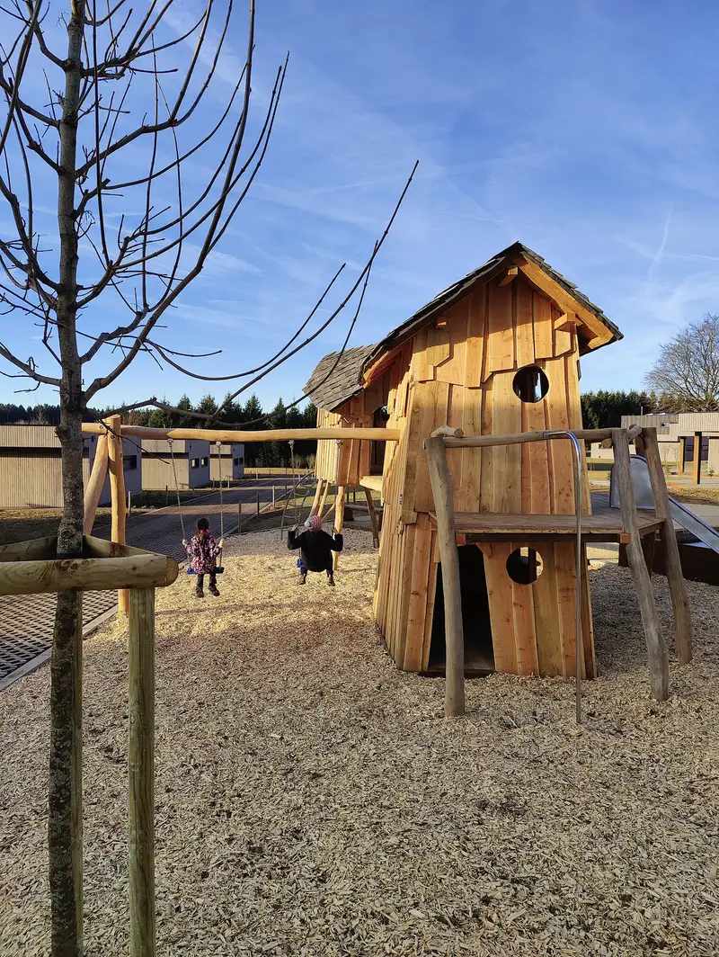 Cabane en bois et balançoires de l'aire de jeux, les villas du village en arrière-plan
