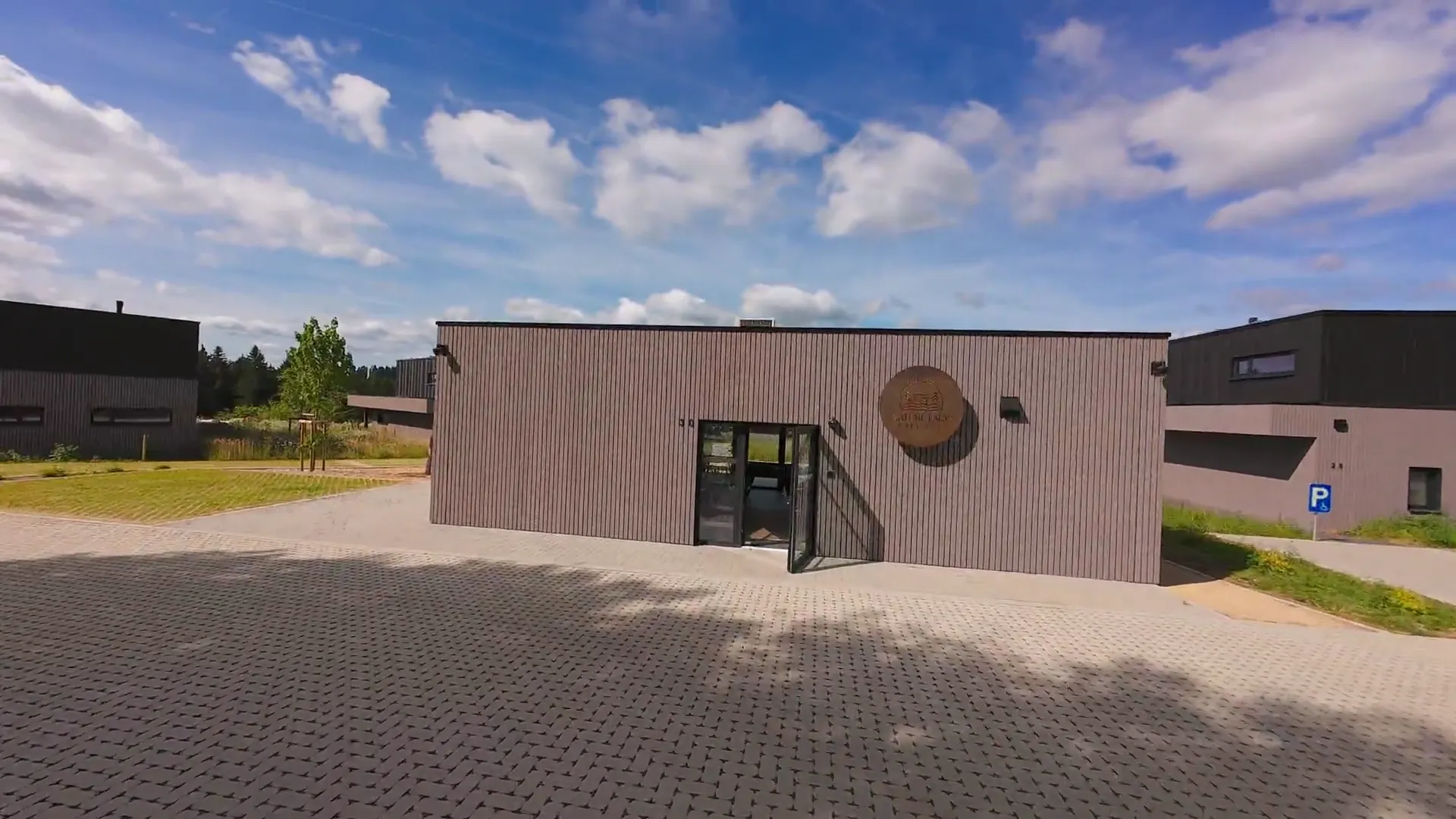 Bâtiment d'accueil de Nature Lake Village avec son enseigne ronde en bois, porte d'entrée ouverte, large allée au premier plan
