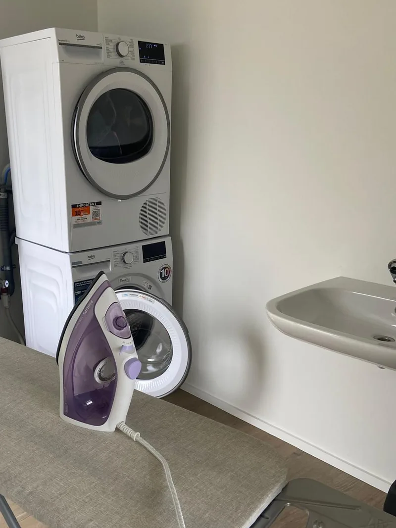 La laverie commune : sèche-linge et machine à laver superposés, table et fer à repasser