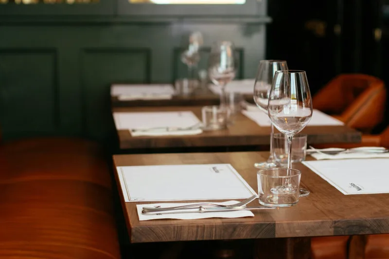 Eingedeckte Restauranttische mit Weingläsern und cognacfarbenen Lederbänken