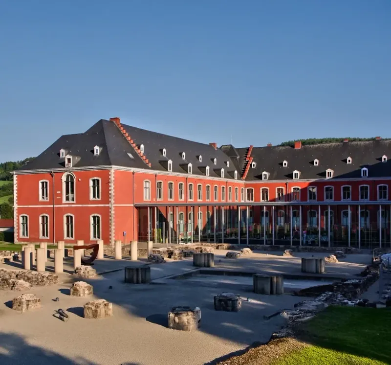 Die Abtei Stavelot mit roten Fassaden, davor die Fundamente der alten Abteikirche