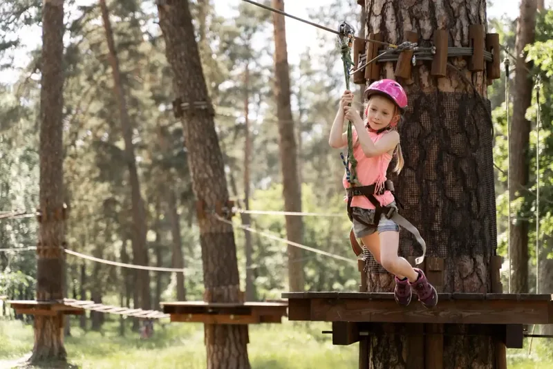 Kind mit Helm auf der Seilrutsche eines Kletterparks zwischen Kiefern