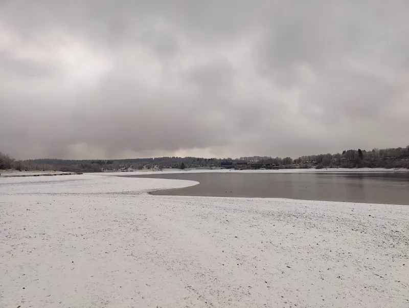 Het strand onder de sneeuw, het dorp aan de overkant van het meer