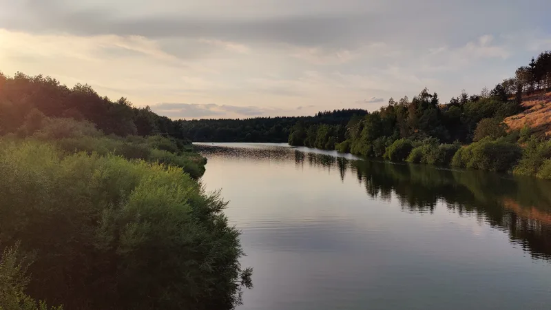 Het spiegelgladde meer tijdens het blauwe uur, de beboste oevers weerspiegelen erin