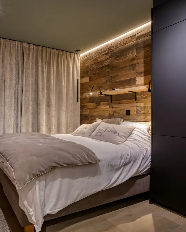 Behagliches Schlafzimmer: Bett an der Altholzwand, stimmungsvolles Licht