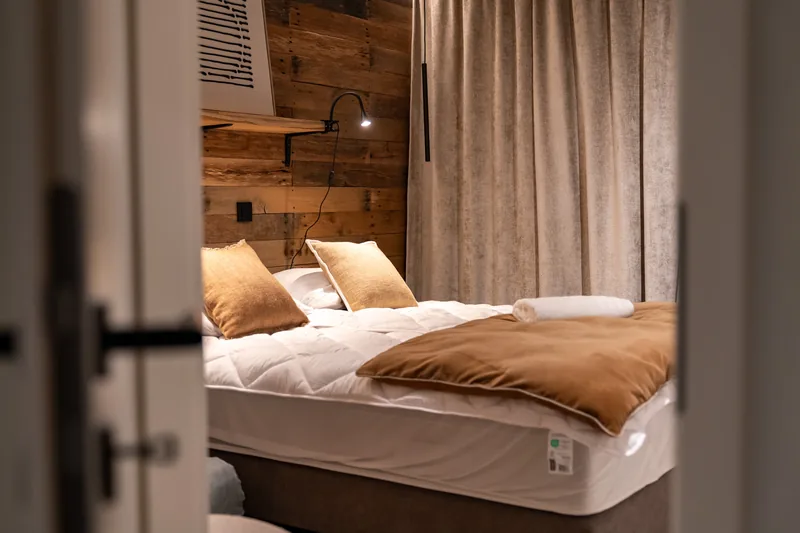 Schlafzimmer mit Kopfteil aus rohem Holz, offene Tür zum Schlafbereich