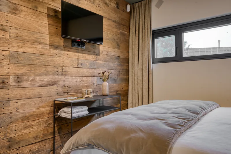 Schlafzimmer mit Wand aus rohem Holz, Wand-TV und Blick auf die Bäume