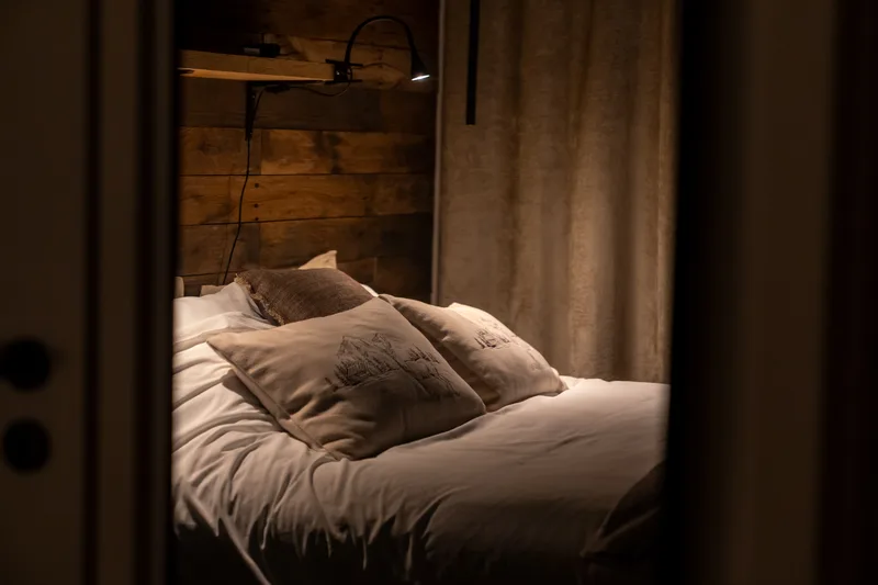 Schlafzimmer am Abend: warmes Licht hinter dem Kopfteil, zugezogene Vorhänge