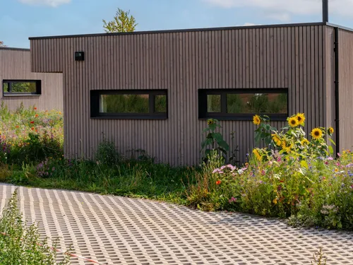 Holzfassade der Villa, davor Sonnenblumen und Wiesenblumen