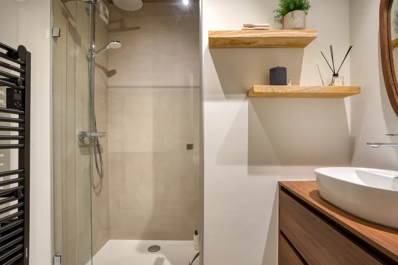 Helles Badezimmer: verglaste Dusche, Steinwaschbecken und Holzregal