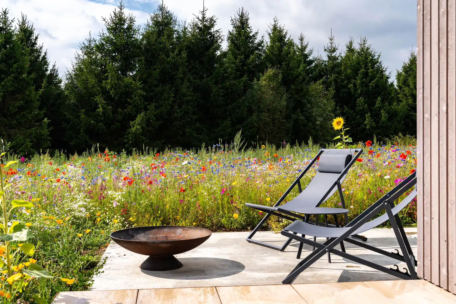 Private Terrasse mit Feuerschale und Liegestühlen vor der Blumenwiese