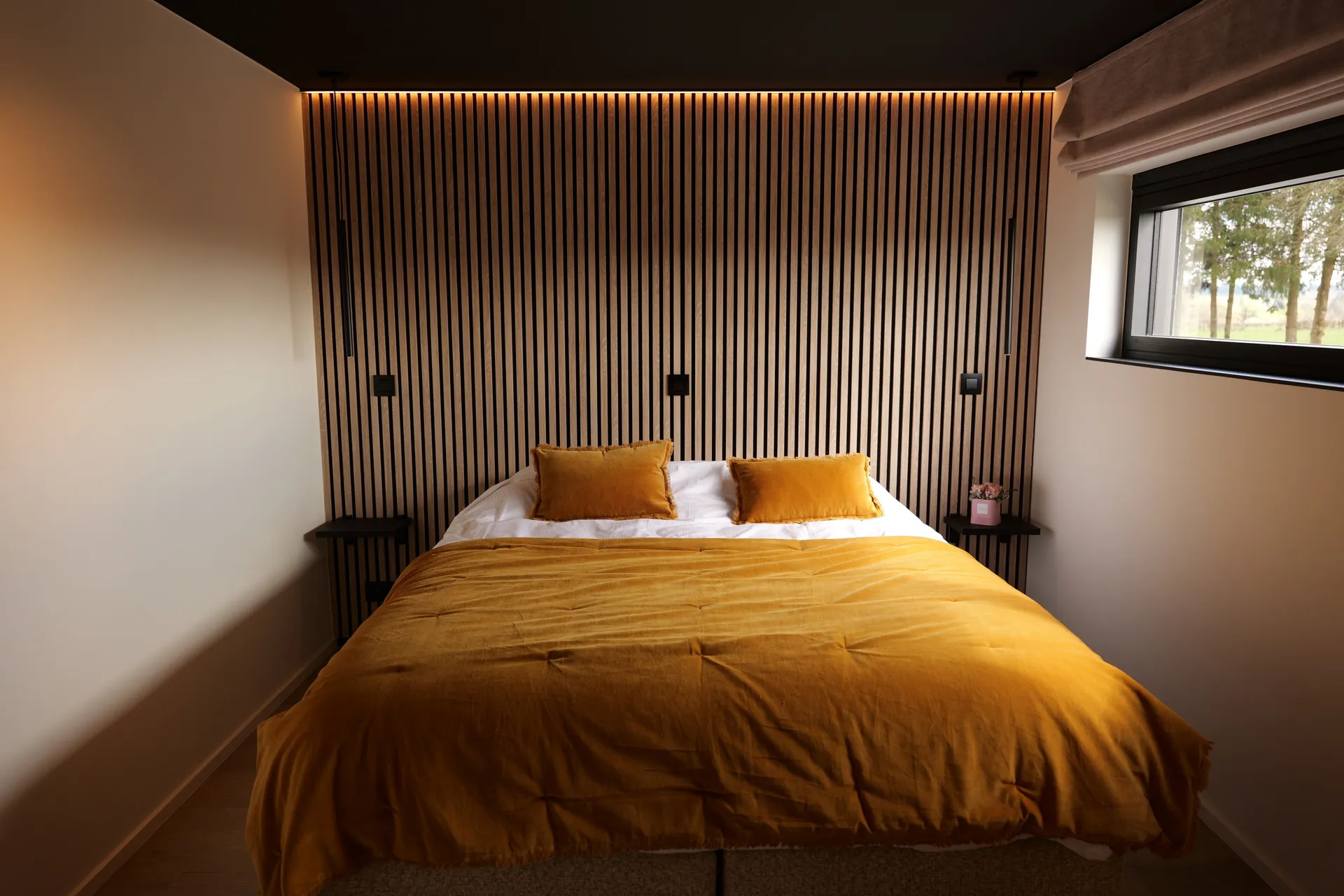 Slaapkamer: bed met mosterdgele sprei voor een verlichte lattenwand