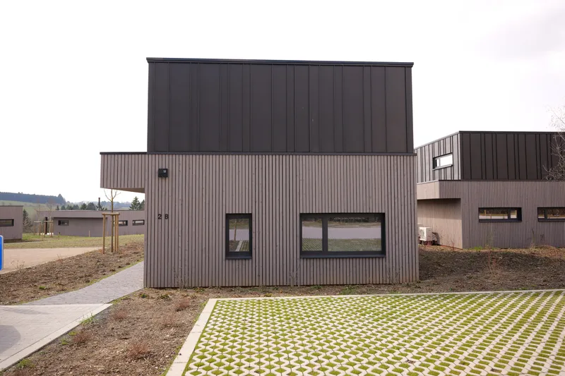 Zijgevel van de villa in houten bekleding, grastegels ervoor