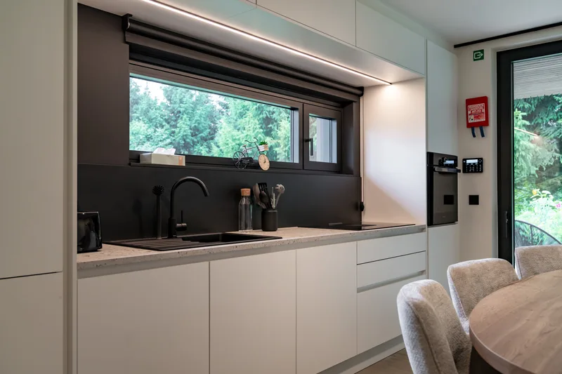 Cuisine équipée, plan de travail noir et fenêtre bandeau sur la prairie