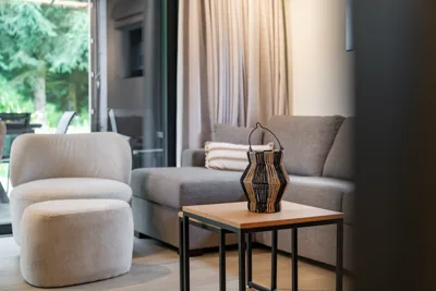 Coin salon cosy : fauteuil en bouclé, lanterne tressée et baie vitrée sur la terrasse, villa 4 chambres