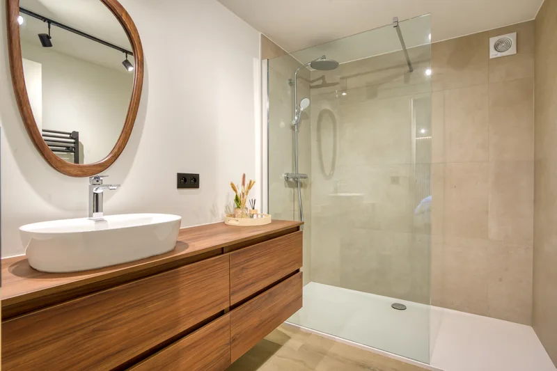Salle de bains : vasque en pierre, miroir ovale et douche à l'italienne