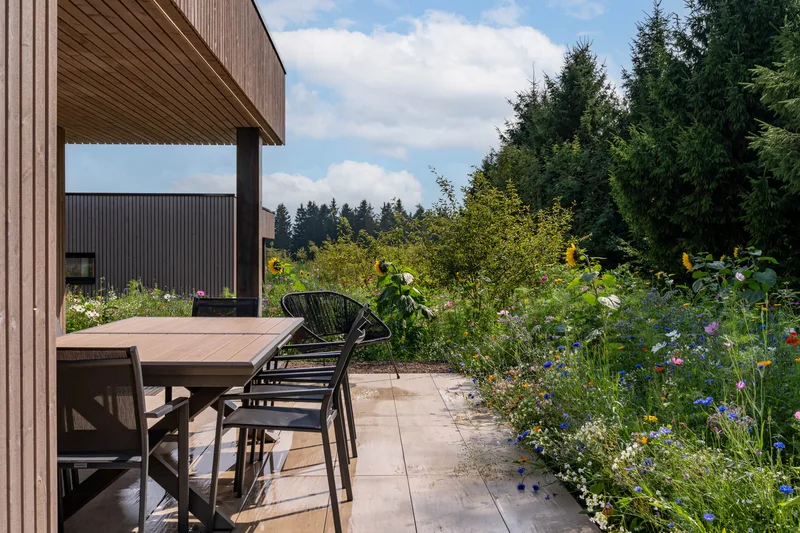 Terrasse en bois avec table à manger, prairie fleurie et sapins en arrière-plan